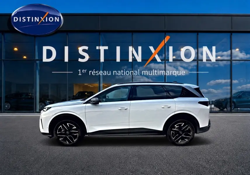 Vue de profil côté gauche d’un Peugeot 5008 Hybrid 145 allure e-dcs6 blanc devant une vitrine Distinxion.