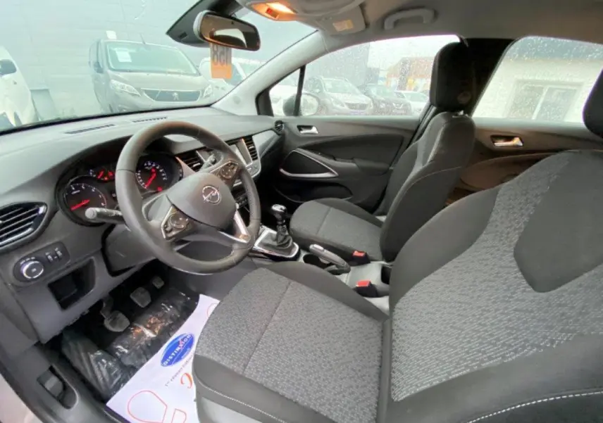 Vue intérieure côté conducteur de l'Opel Crossland gris, montrant le volant cuir, tableau de bord et sièges tissu gris.