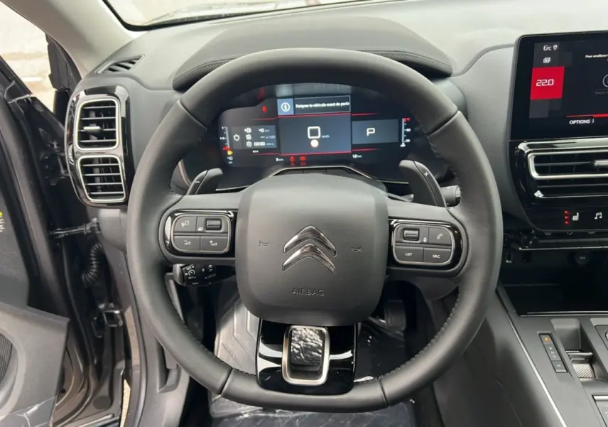 Vue intérieure centrée sur le volant du Citroën C5 Aircross Hybrid 2025, avec tableau de bord numérique et commandes intégrées.