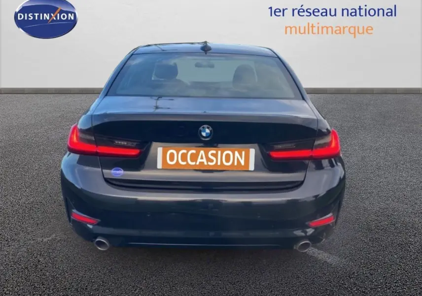 Vue arrière d'une BMW Série 3 G20 noire de 2019 avec feux arrière allumés et double sortie d'échappement.