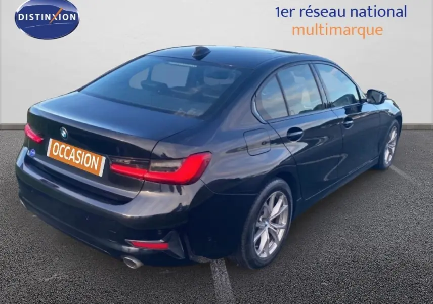 BMW Série 3 G20 noire vue 3/4 arrière droit, avec jantes alliage 17 pouces et feux arrière allumés.