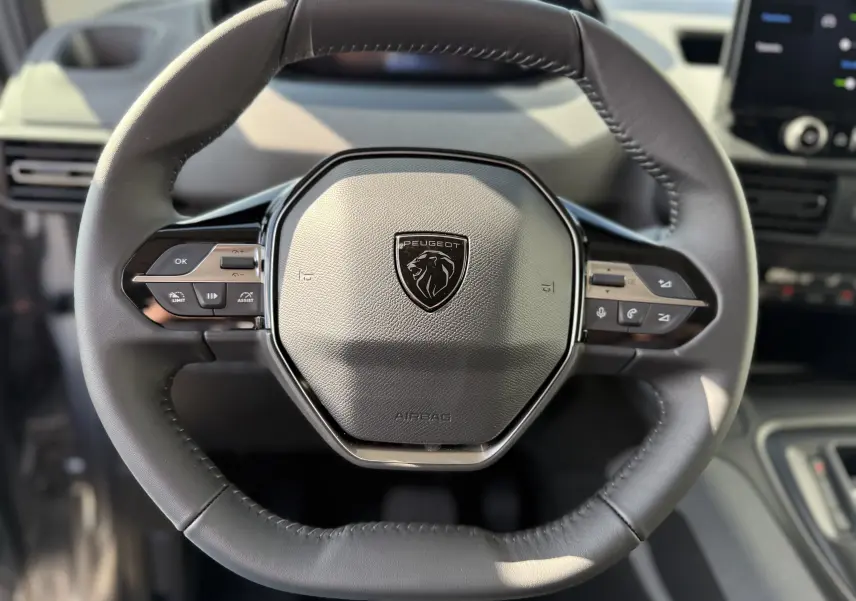 Gros plan sur le volant cuir noir du Peugeot Rifter Allure 2026 avec commandes intégrées et logo lion central.