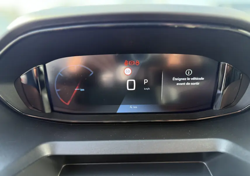 Tableau de bord numérique du Peugeot Rifter Allure 2026, affichant la vitesse à 0 km/h et un message d'alerte.