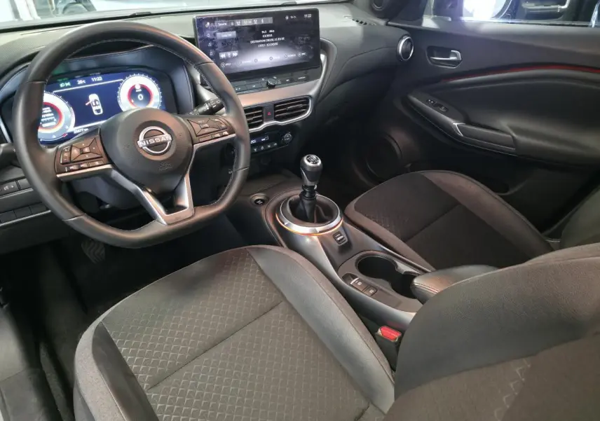 Vue intérieure côté conducteur du Nissan Juke 2025 gris, volant cuir, écran tactile 12,3 pouces et boîte manuelle.