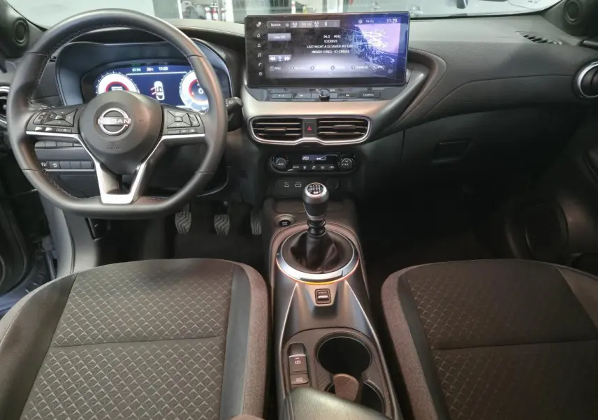 Vue intérieure avant du Nissan Juke 2025 avec volant cuir, écran tactile central 12,3 pouces et levier de vitesses manuel.
