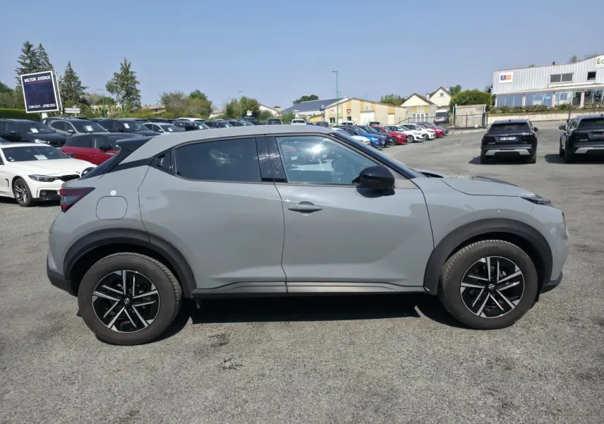 Vue de profil côté gauche d'un Nissan Juke gris métallisé 2025 avec jantes alliage noires et toit noir.