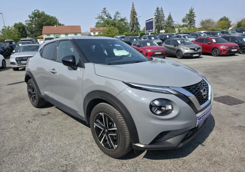 Nissan Juke gris métallisé vue 3/4 avant droit avec jantes alliage noires et coques de rétroviseurs noires.