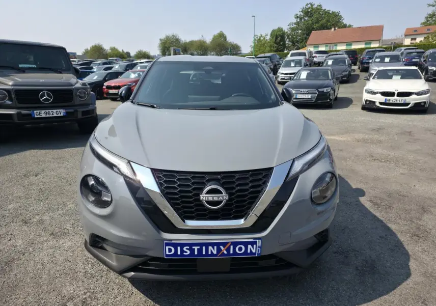 Vue avant d'un Nissan Juke gris métallisé 2025 avec calandre en V chromée et logo Nissan visible.
