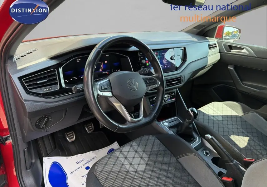 Vue intérieure côté conducteur d’une Volkswagen Polo rouge Roi 2023, volant multifonctions et tableau de bord digital visibles.