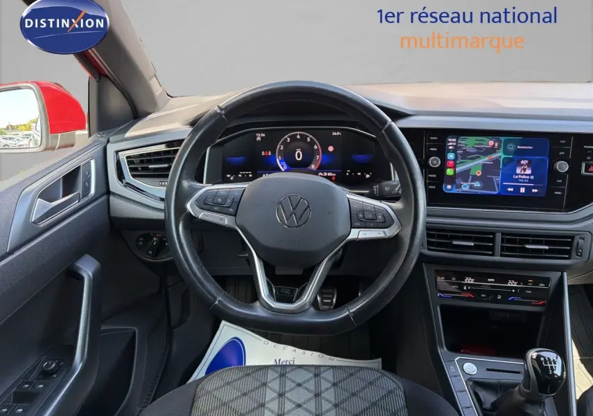 Vue intérieure centrée sur le volant et tableau de bord d'une Volkswagen Polo rouge Roi avec boîte manuelle, écran tactile et climatisation.
