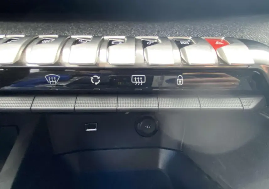 Gros plan sur la rangée de commandes chromées et la prise 12V du tableau de bord du Peugeot 3008 Allure blanc nacré 2017.