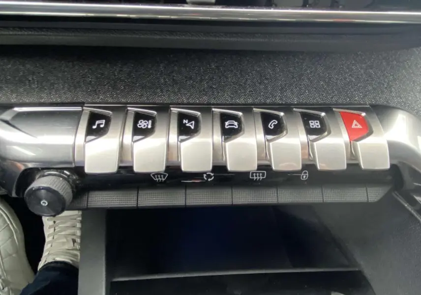 Gros plan sur la rangée de boutons argentés du tableau de bord du Peugeot 3008 blanc, avec commande de musique et alertes.