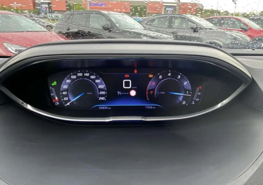 Tableau de bord numérique du Peugeot 3008 blanc 2017, affichant vitesse et compte-tours, avec pluie en arrière-plan.