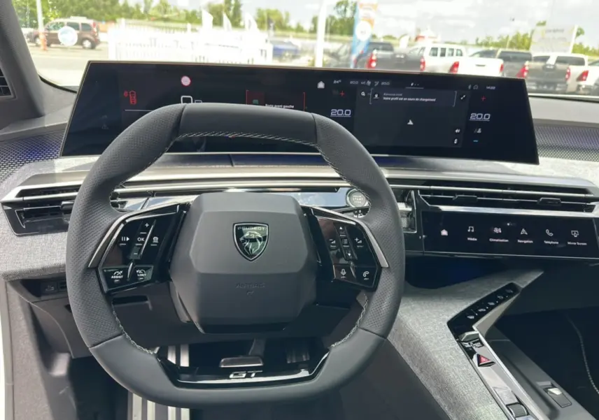 Vue intérieure centrée sur le volant cuir multifonctions et le tableau de bord numérique du Peugeot 5008 Hybrid GT.
