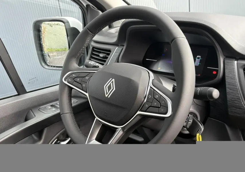 Vue intérieure rapprochée du volant multifonction Renault Trafic Fourgon, avec tableau de bord numérique et rétroviseur côté gauche.