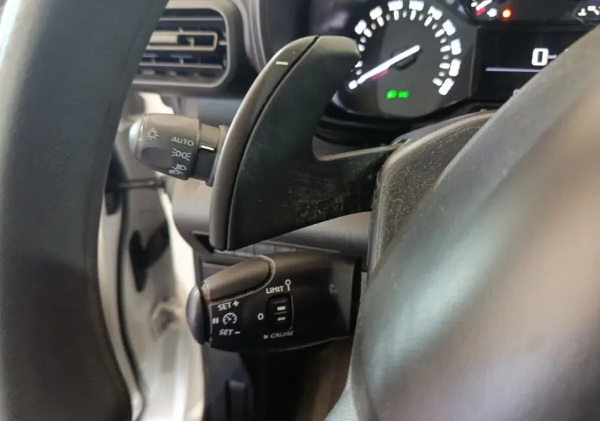 Gros plan sur la commande de régulateur de vitesse et palettes au volant d’un Citroën Berlingo blanc, vue côté gauche.