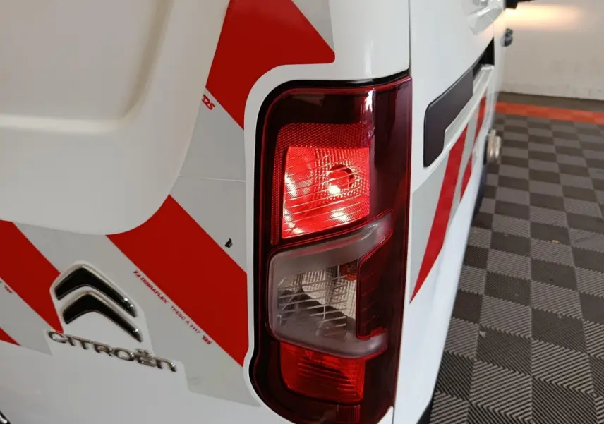 Gros plan sur le feu arrière droit d’un Citroën Berlingo blanc 2021 avec marquages rouges en diagonale.