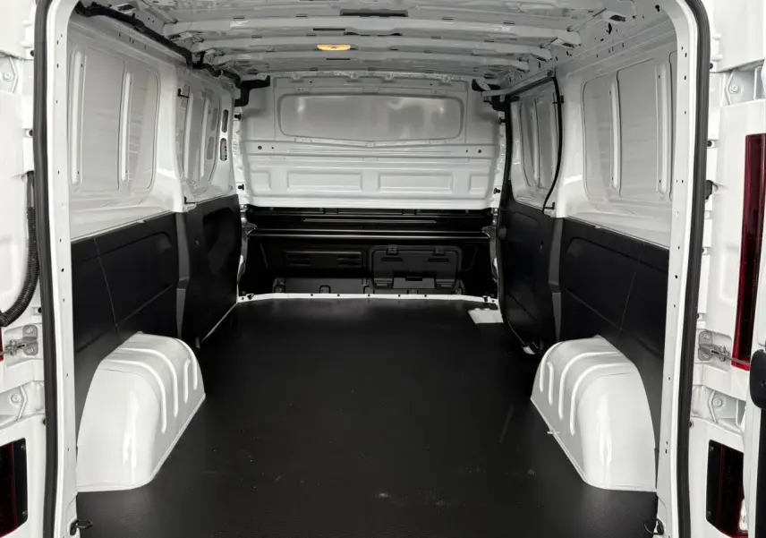 Vue intérieure arrière du Renault Trafic Fourgon blanc Glacier, montrant l'espace de chargement avec plancher bois noir.