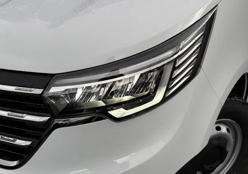 Gros plan sur le phare avant droit LED du Renault Trafic Fourgon blanc Glacier avec calandre noire et jante acier.