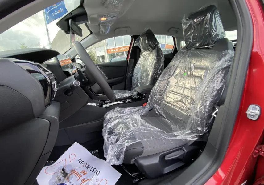 Vue intérieure côté conducteur de la Citroën C4 2023 rouge Elixir avec sièges protégés par film plastique.
