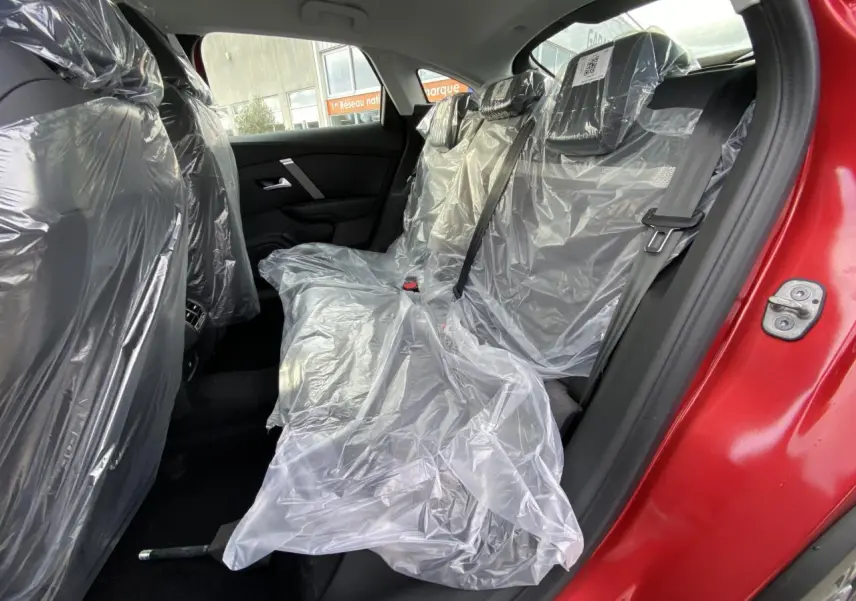 Vue côté gauche arrière de l'intérieur d'une Citroën C4 rouge Elixir, sièges arrière protégés par housses plastiques.