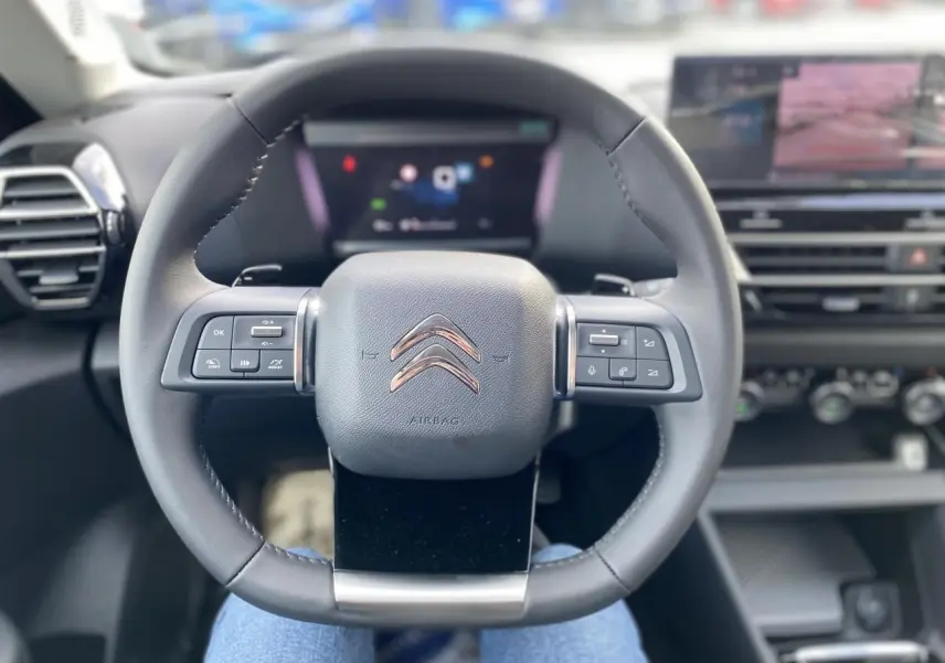 Vue centrée sur le volant du Citroën C4 2023, intérieur noir avec commandes intégrées et écran digital flou.