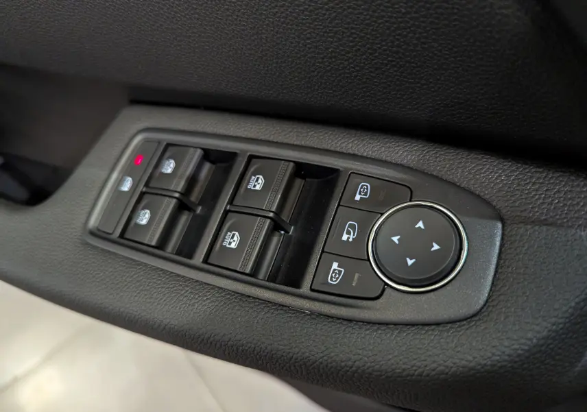 Gros plan sur les commandes des vitres et rétroviseurs côté conducteur d'une Renault Clio V, finition tissu noire.