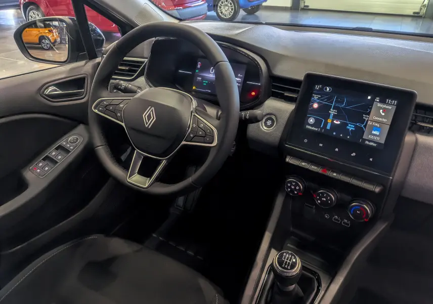 Vue intérieure côté conducteur de la Renault Clio V gris Rafale, avec volant multifonction, écran tactile et boîte manuelle.