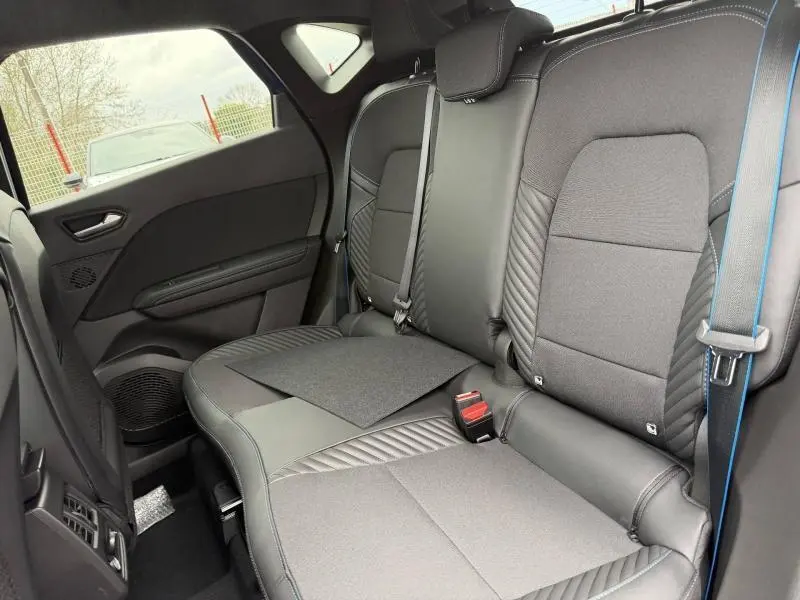 Vue intérieure arrière droite du Renault Captur 2026, sièges noirs avec surpiqûres bleu électrique et ceinture assortie.