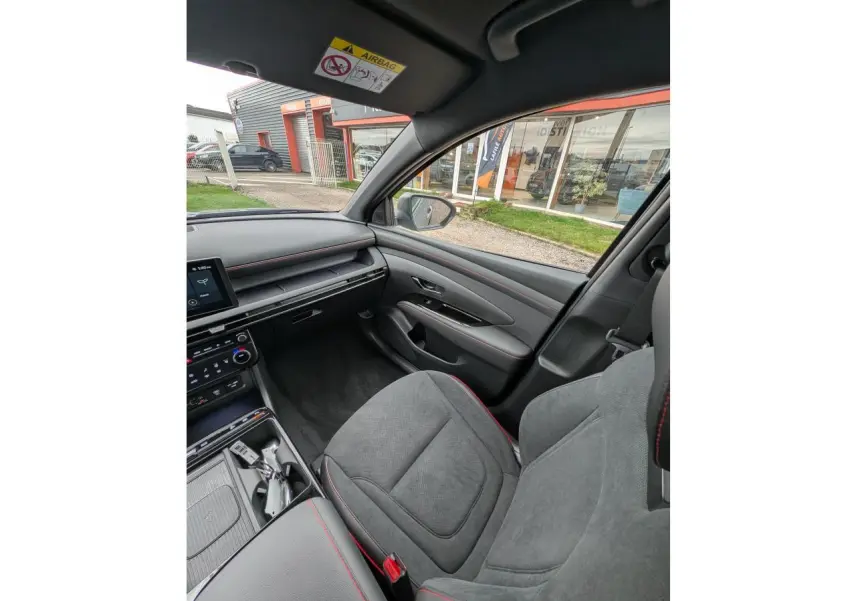 Vue intérieure côté passager du Hyundai Tucson gris, sellerie cuir/alcantara gris avec surpiqûres rouges et planche de bord noire.