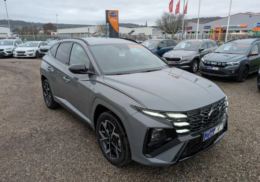 Vue 3/4 avant d'un Hyundai Tucson gris métallisé avec calandre noire N Line et jantes alliage 19 pouces sur parking.