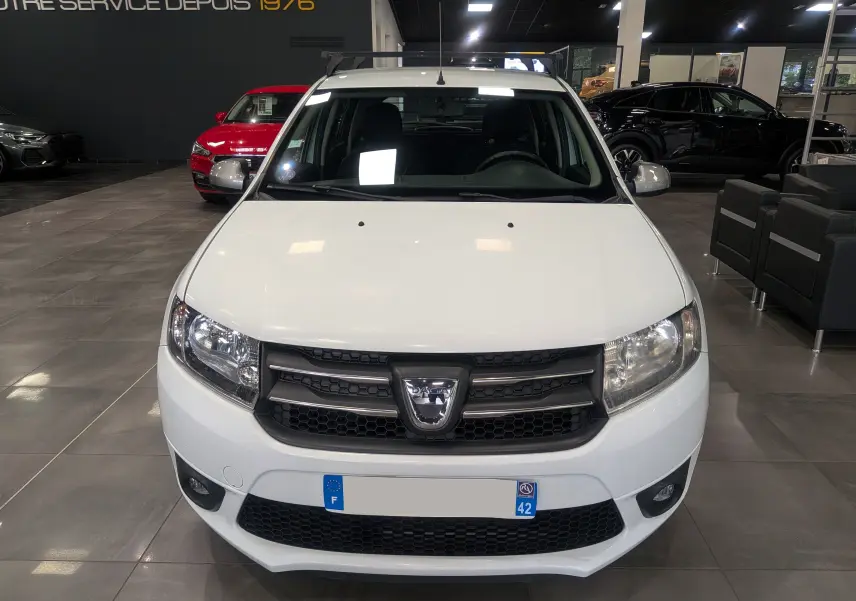 Vue frontale d'une Dacia Sandero TCe 90 CH SL 10 ANS blanc glacier en showroom avec calandre noire et phares allumés.