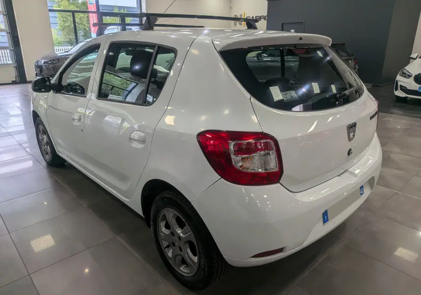 Vue 3/4 arrière droite d'une Dacia Sandero blanc glacier en intérieur, avec jantes alliage et vitres teintées.