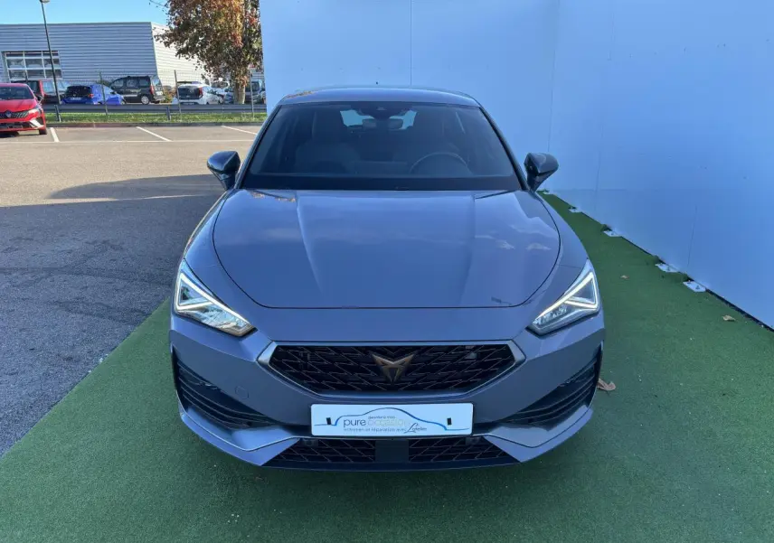 Vue frontale d'une CUPRA Leon 2024 gris Graphene avec calandre noire et feux LED anguleux allumés.