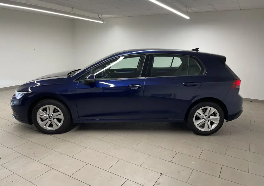 Profil côté gauche d'une Volkswagen Golf 1.0 TSI 110 DSG7 Life Plus 2023 en bleu Atlantique métallisé, en intérieur.
