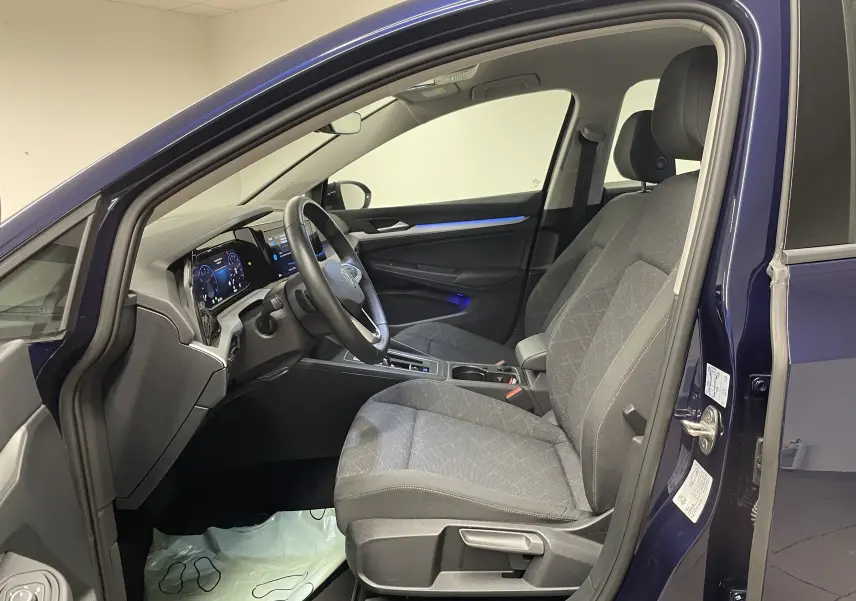 Vue intérieure côté conducteur d'une Volkswagen Golf 2023 Bleu Atlantique avec sièges tissu gris et tableau de bord digital.