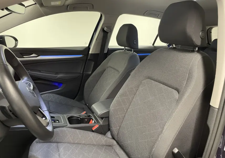 Intérieur de la Volkswagen Golf 2023, vue côté gauche sur les sièges avant gris et l'éclairage d'ambiance bleu.