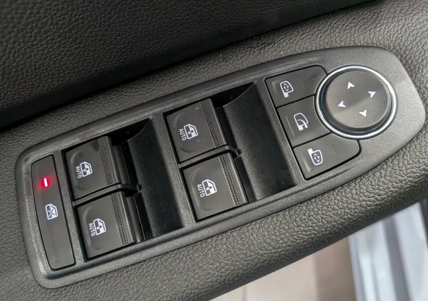 Gros plan sur les commandes de lève-vitres et rétroviseurs électriques noires dans l'habitacle d'une Renault Clio V gris Rafale.