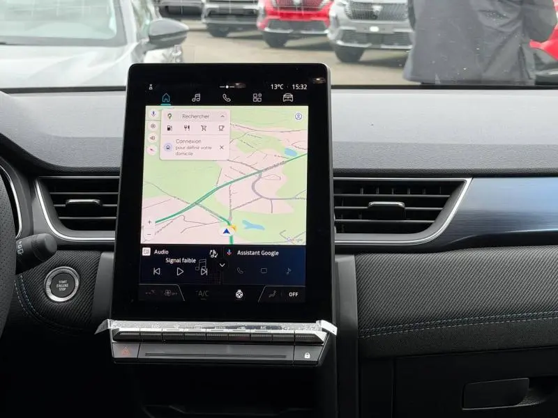 Vue intérieure centrée sur l'écran tactile vertical du tableau de bord du Renault Captur blanc nacré 2026, avec détails carbone et surpiqûres bleues.