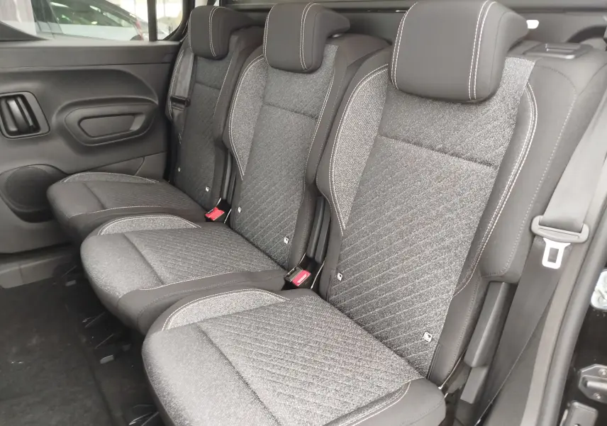 Vue intérieure du siège arrière droit du Peugeot Rifter 2026 noir Perla Nera, avec trois sièges en tissu gris à surpiqûres blanches.