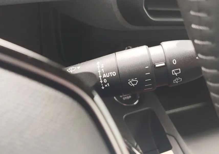 Gros plan sur la manette d'essuie-glace noire à droite du volant dans l'habitacle du Peugeot Rifter noir.