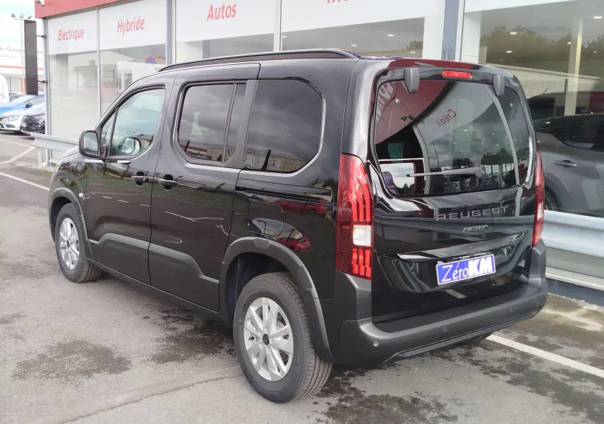 Vue 3/4 arrière droite d’un Peugeot Rifter noir Perla Nera avec vitres teintées et feux arrière verticaux allumés.