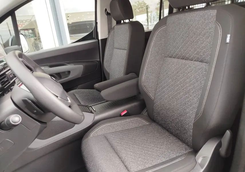 Vue intérieure côté conducteur du Peugeot Rifter 2026, sièges gris tissu avec coutures contrastées et accoudoir central.