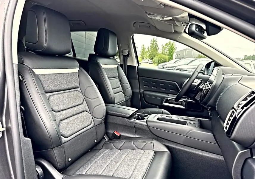 Vue intérieure côté conducteur du Citroën C5 Aircross 2025, sièges tissu brun et cuir noir avec console centrale visible.