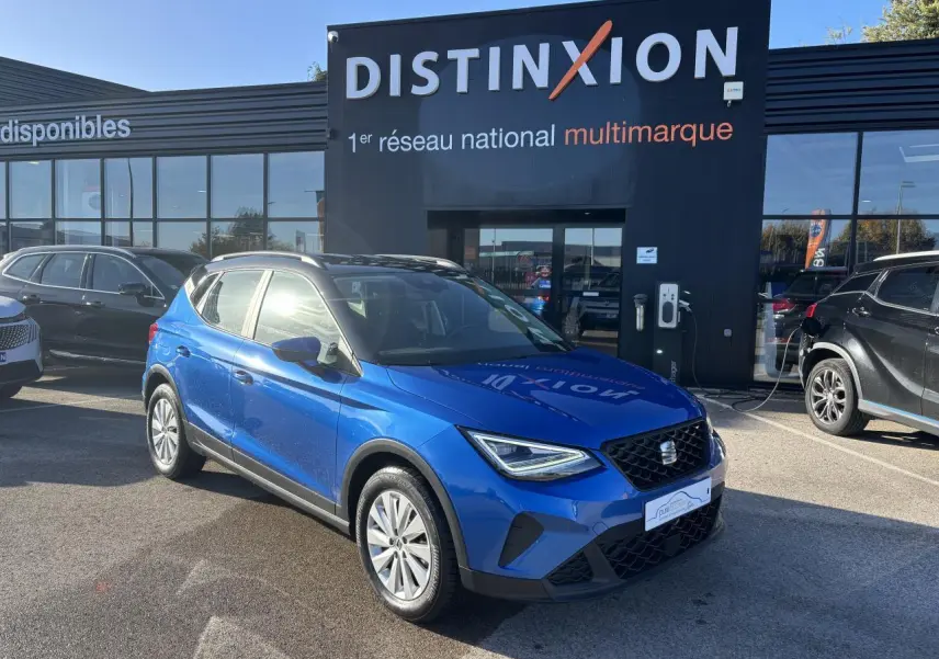 Vue 3/4 avant d'un SEAT Arona bleu saphir avec toit noir, stationné devant un bâtiment Distinxion.