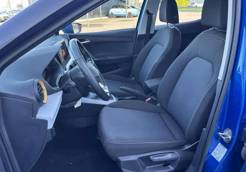 Vue intérieure côté conducteur du SEAT Arona bleu saphir, montrant les sièges tissu et le tableau de bord avec écran tactile.