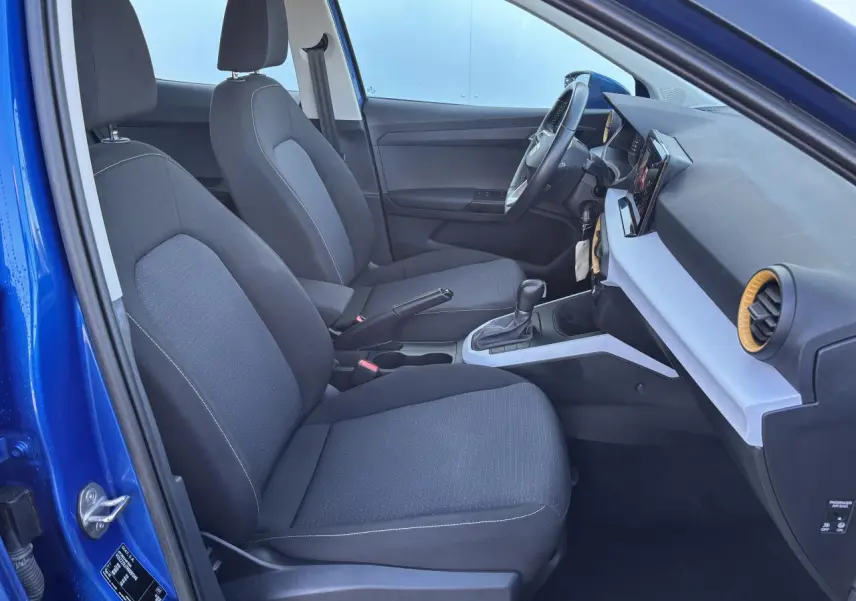 Vue intérieure côté conducteur de la SEAT Arona bleu saphir, montrant les sièges tissu et la console centrale moderne.
