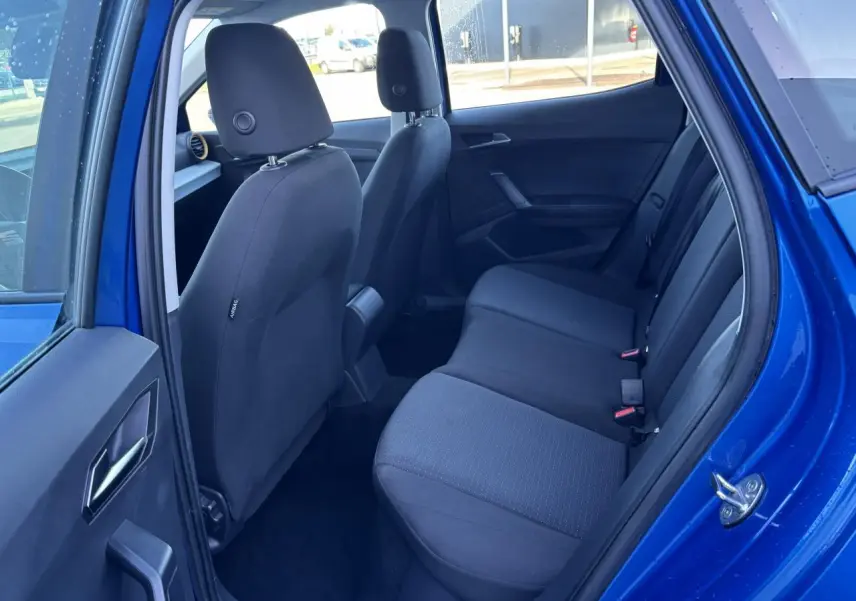 Vue côté droit de l'habitacle arrière du SEAT Arona bleu saphir, montrant les sièges en tissu noir et la porte ouverte.