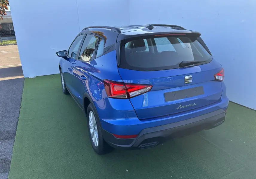 Vue 3/4 arrière d’un SEAT Arona bleu saphir avec toit noir, jantes alliage et barres de toit noires.