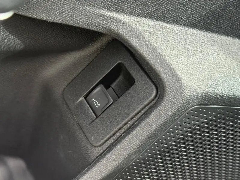 Gros plan sur le bouton d'ouverture du coffre noir dans l'habitacle du CUPRA Formentor bleu 2025.